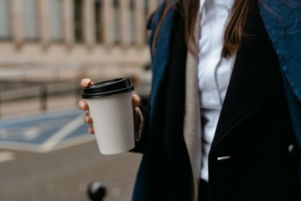 Woman in formal attire holding a takeaway coffee cup on a city street.
